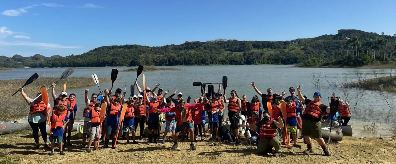 Scouts in orange life vests with paddles raised on the lake at Guajataka